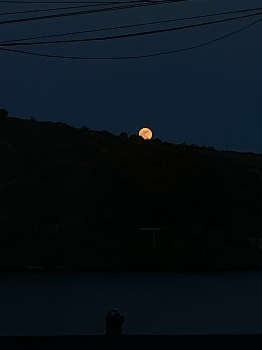 A full moon rising over a dark hillside above the water at dusk