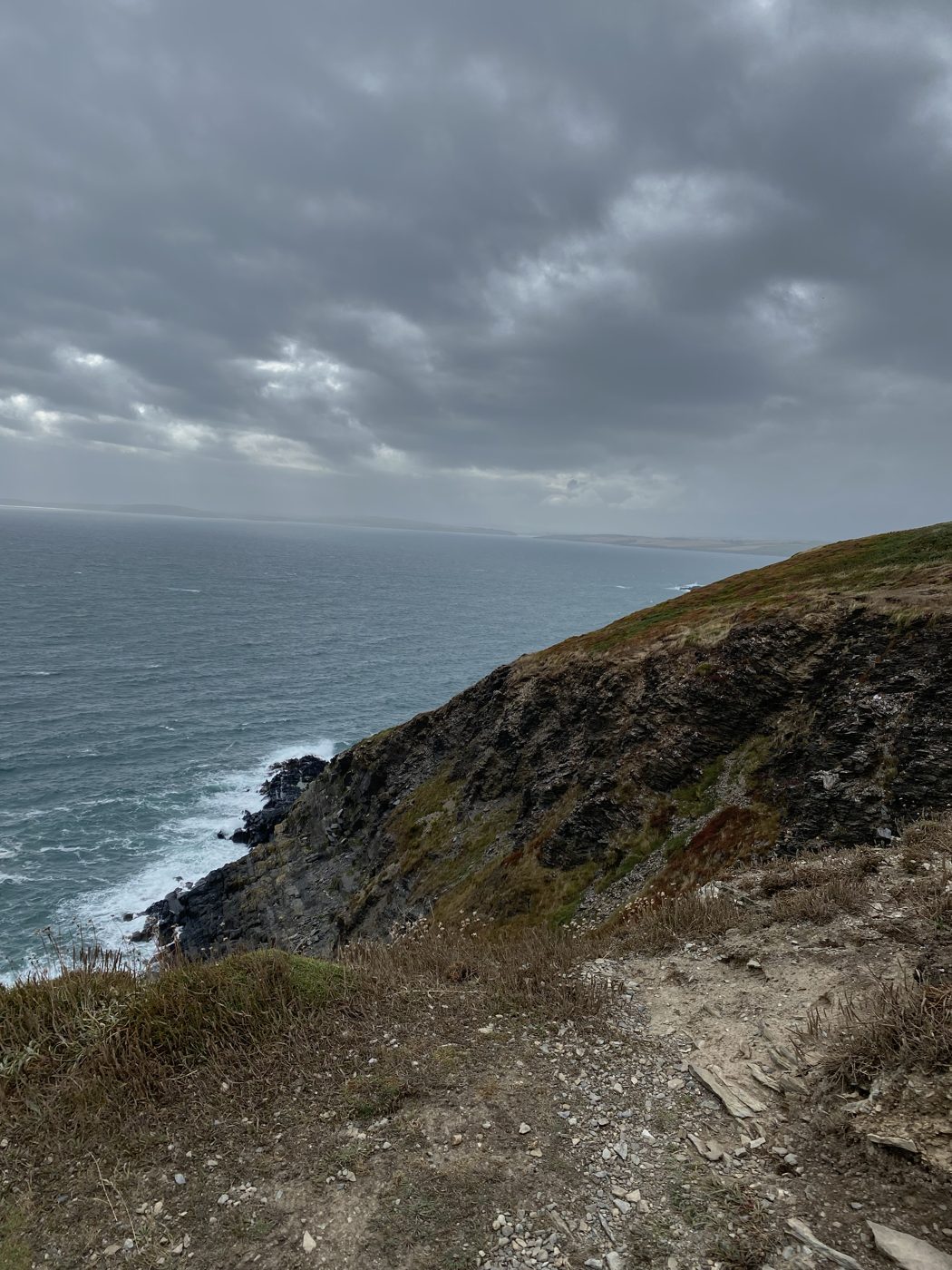 Waves against rugged green coastal cliffs under a cloudy sky