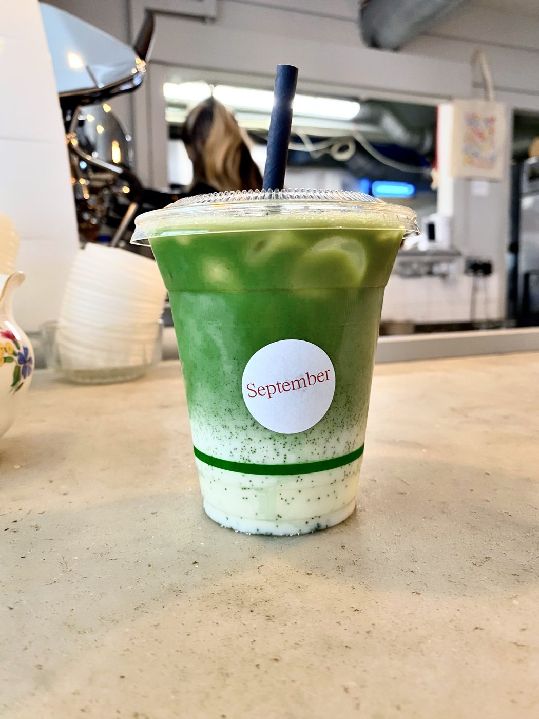 An iced matcha drink labelled September on a cafe counter